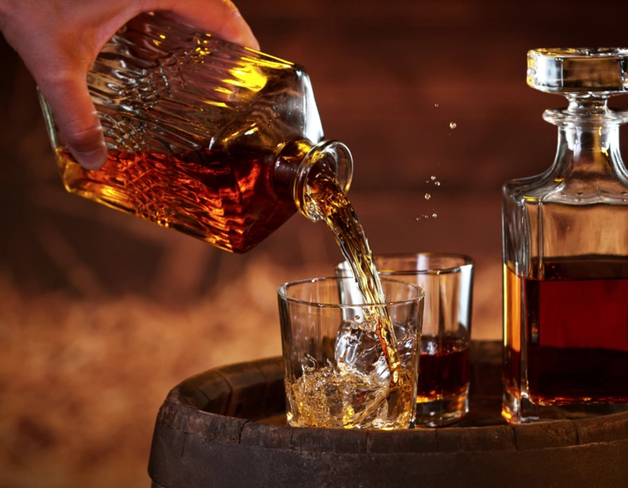man pouring whisky from whiskey decanter into glass