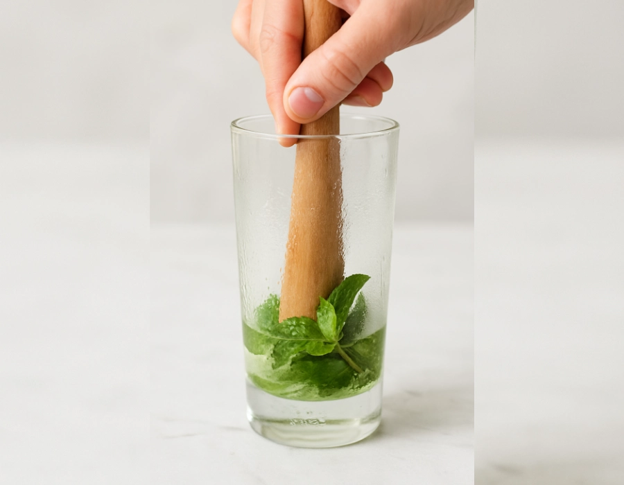 Close-up of fresh mint being muddled in a tall glass